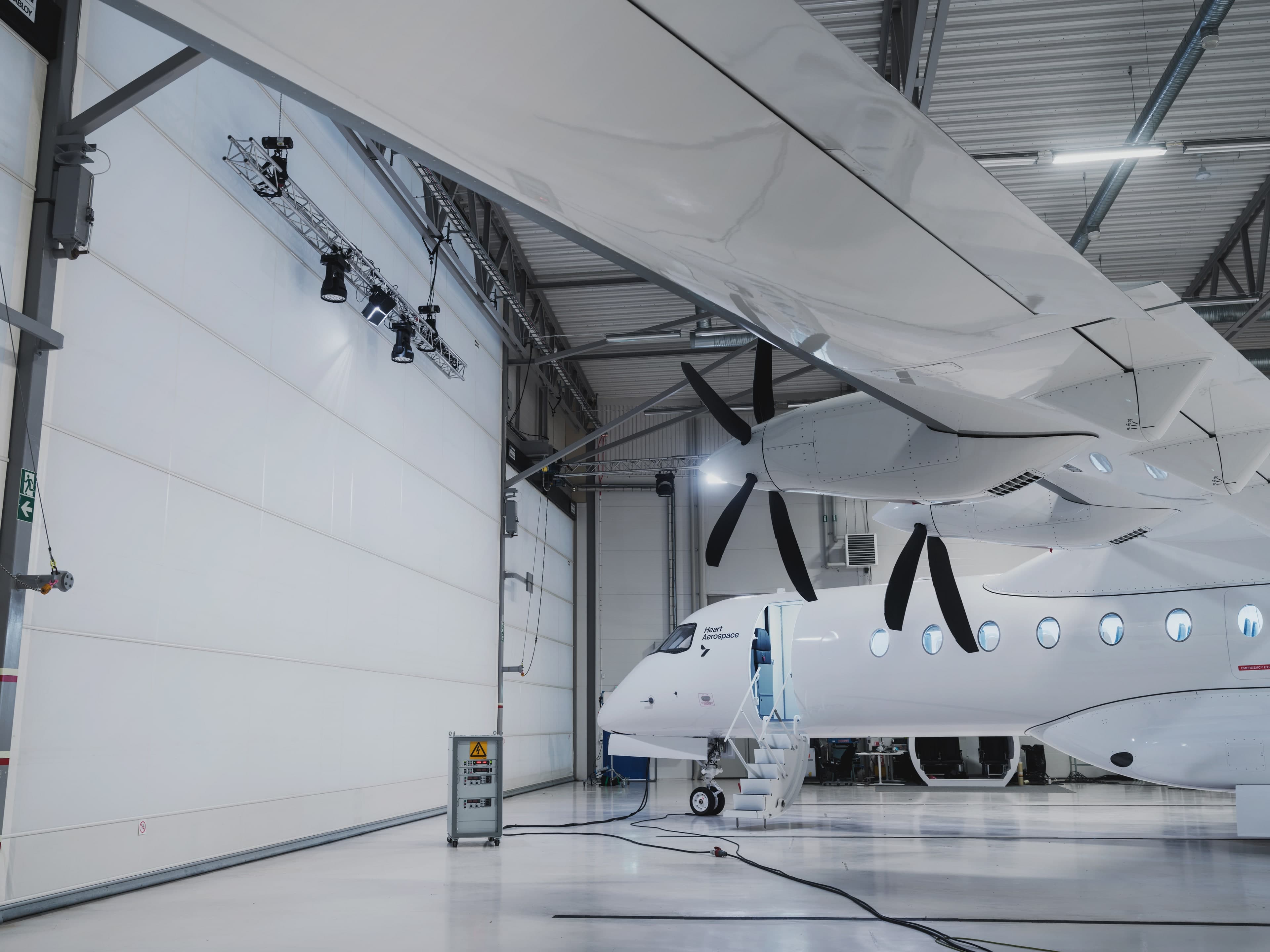 Heart Aerospace X1 prototype inside the hangar — wing and propellers seen from below in bright daylight
