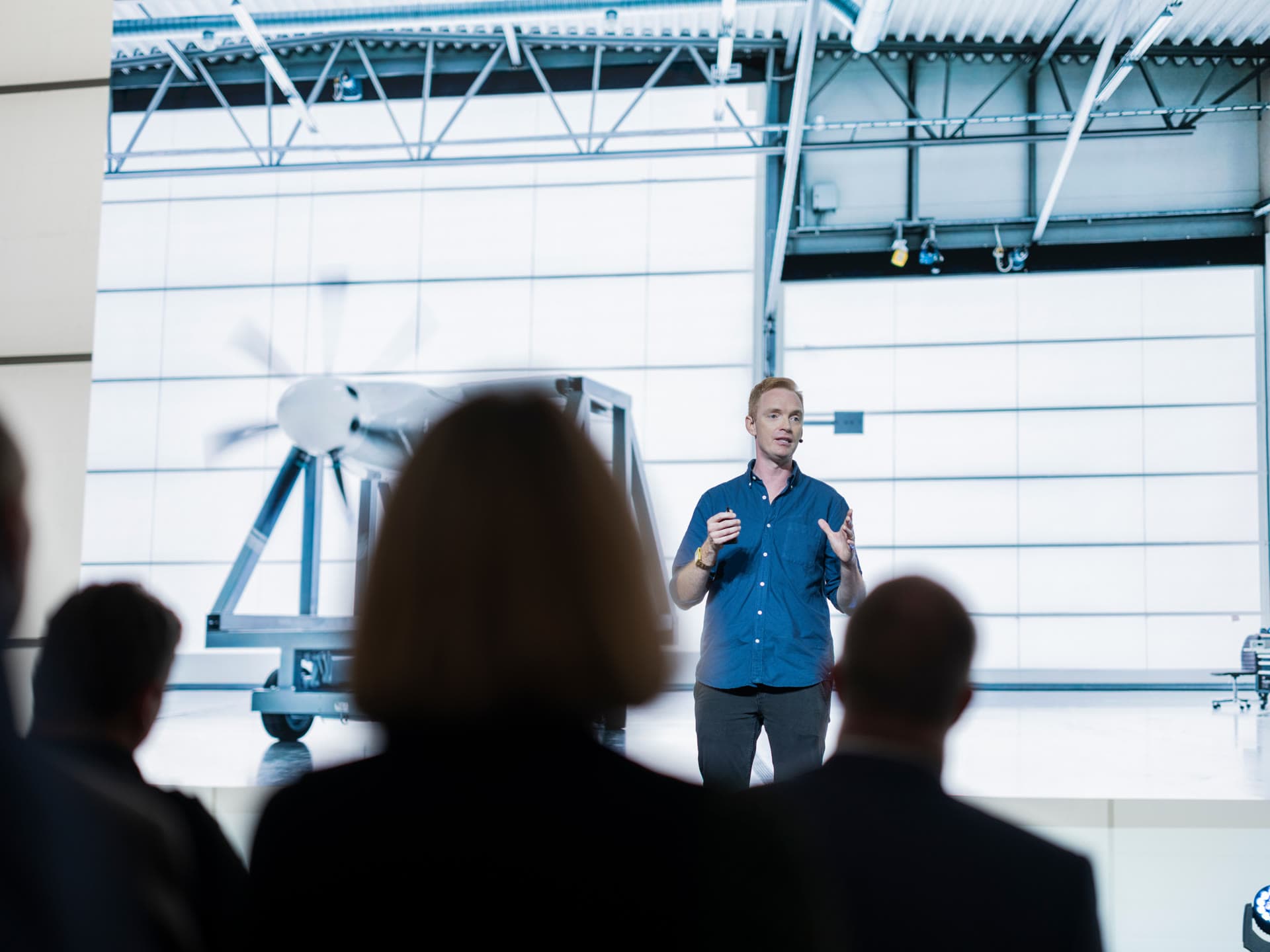 Speaker on stage at Hangar Day 2022 with an electric propulsion demonstrator behind and the audience in the foreground